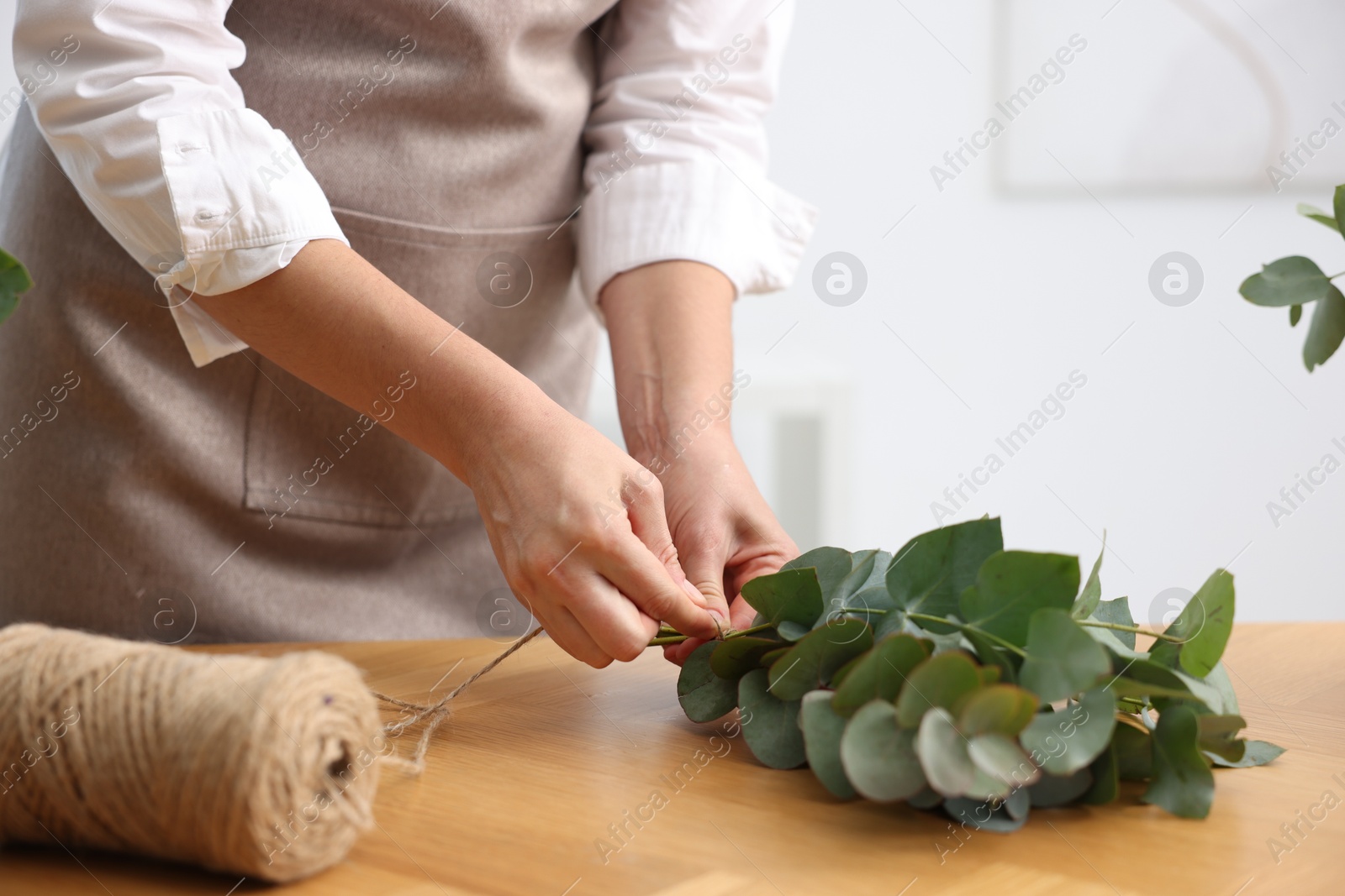Photo of Florist making beautiful bouquet of eucalyptus branches at wooden table in flower shop, closeup