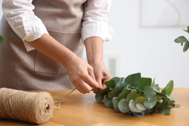 Photo of Florist making beautiful bouquet of eucalyptus branches at wooden table in flower shop, closeup