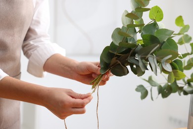 Photo of Florist making beautiful bouquet of eucalyptus branches in flower shop, closeup