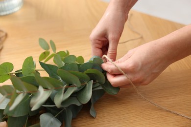 Photo of Florist making beautiful bouquet of eucalyptus branches at wooden table in flower shop, closeup