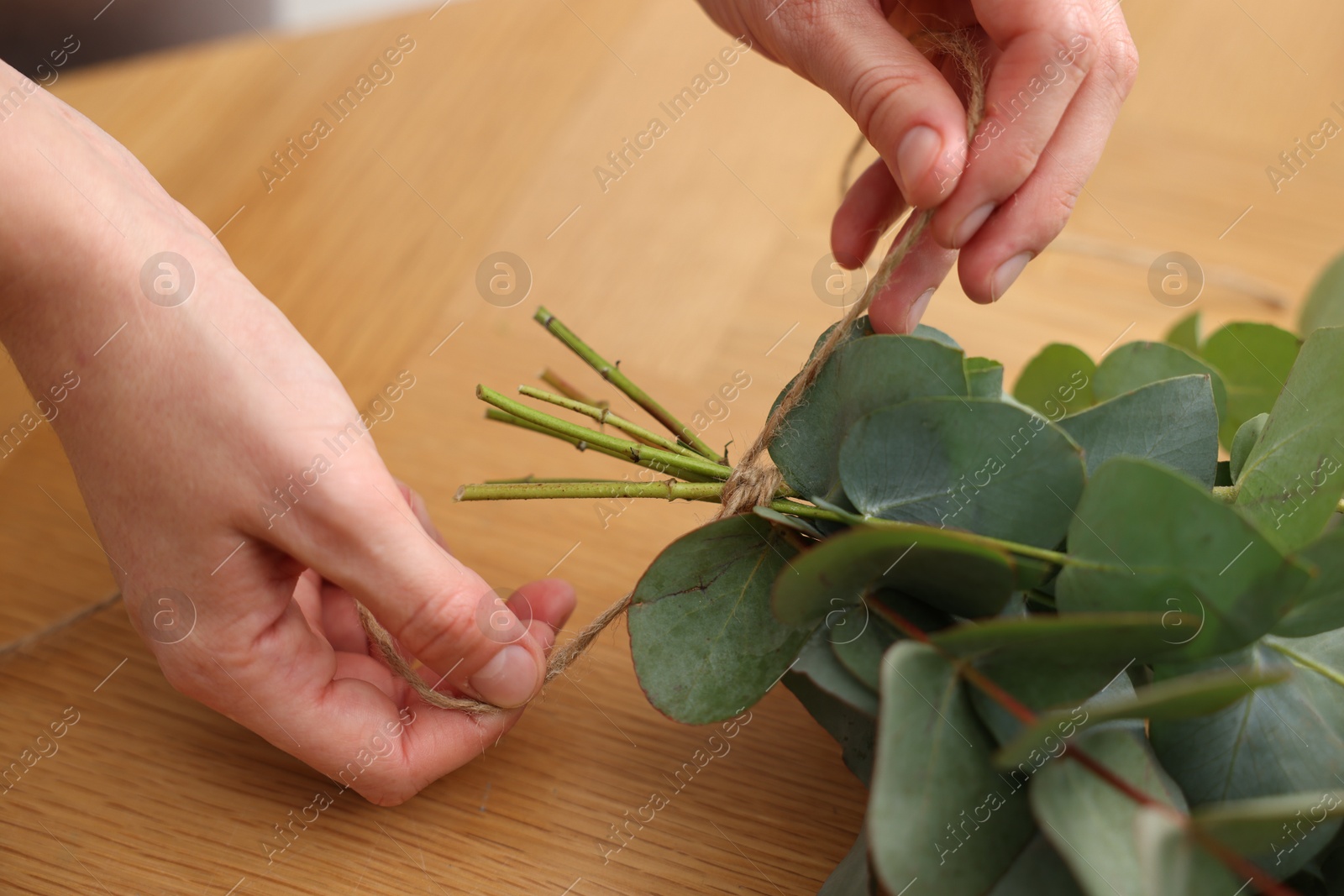 Photo of Florist making beautiful bouquet of eucalyptus branches at wooden table in flower shop, closeup