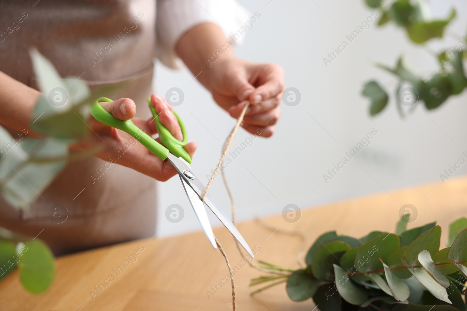 Photo of Florist making beautiful bouquet of eucalyptus branches at wooden table in flower shop, closeup