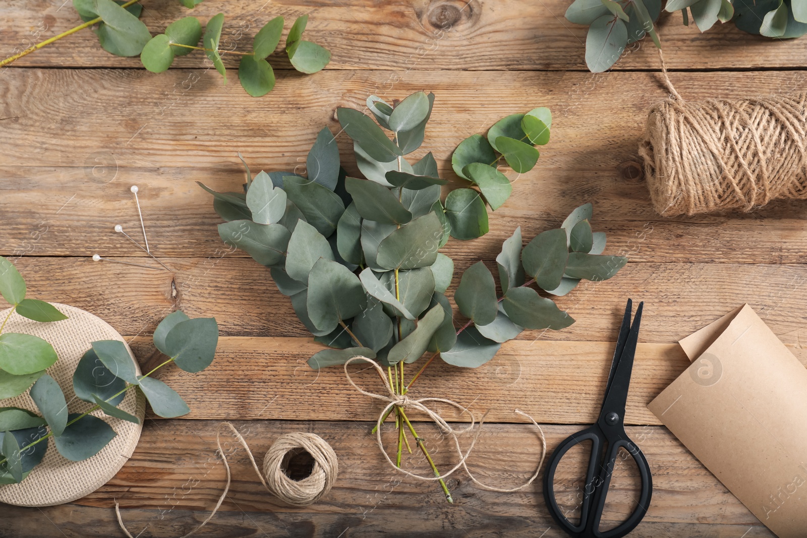 Florist. Eucalyptus branches, threads, pins, scissors and wrapping paper on wooden table, flat lay Photo of Florist. Eucalyptus branches, threads, pins, scissors and wrapping paper on wooden table, flat lay
