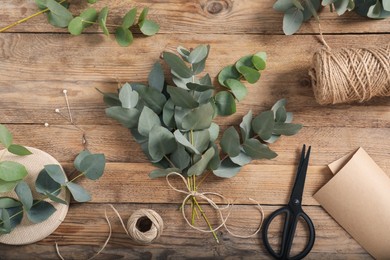 Photo of Florist. Eucalyptus branches, threads, pins, scissors and wrapping paper on wooden table, flat lay
