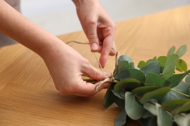 Photo of Florist making beautiful bouquet of eucalyptus branches at wooden table in flower shop, closeup