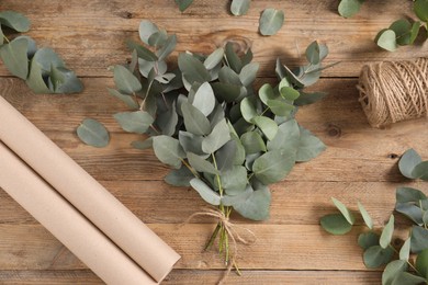 Photo of Florist. Eucalyptus branches, thread and wrapping paper on wooden table, flat lay