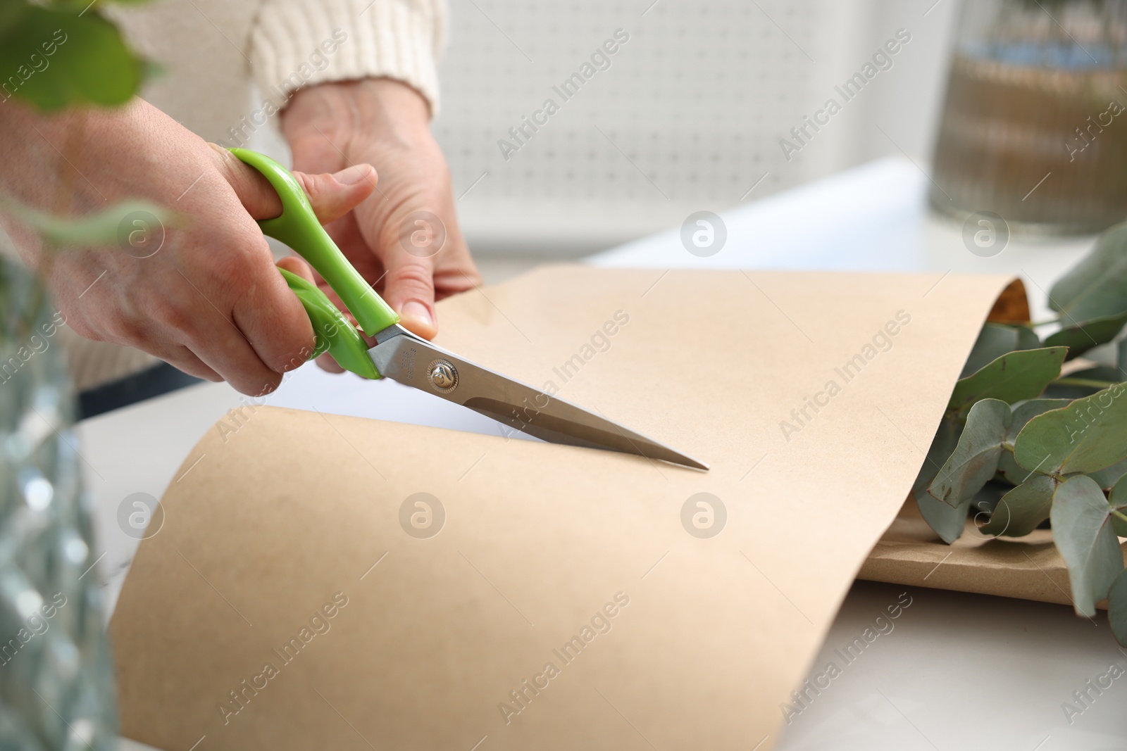 Photo of Florist making beautiful bouquet of eucalyptus branches at white table in flower shop, closeup
