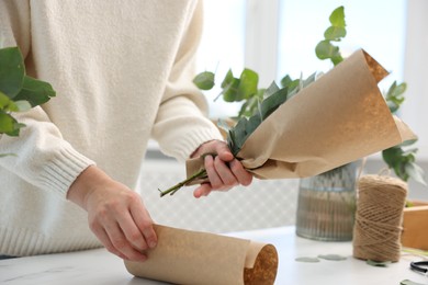 Photo of Florist making beautiful bouquet of eucalyptus branches at white marble table in flower shop, closeup
