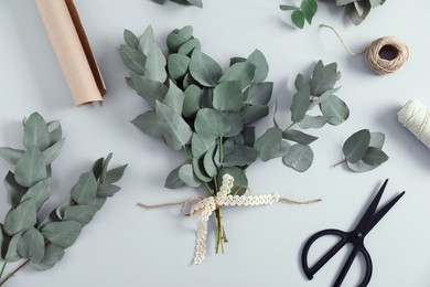 Photo of Florist. Eucalyptus branches, threads, wrapping paper and scissors on white table, flat lay