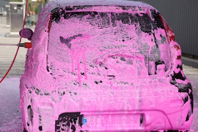 Photo of Auto covered with cleaning foam at outdoor car wash, closeup