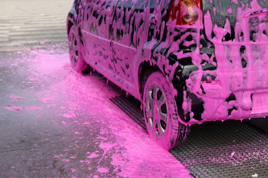Photo of Auto covered with cleaning foam at outdoor car wash, closeup