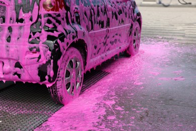 Photo of Auto covered with cleaning foam at outdoor car wash, closeup