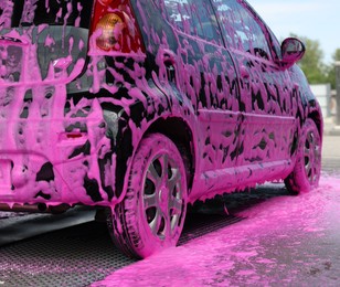 Photo of Auto covered with cleaning foam at outdoor car wash, closeup