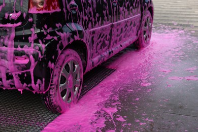 Photo of Auto covered with cleaning foam at outdoor car wash, closeup
