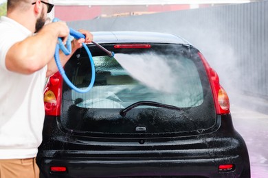 Photo of Man washing auto with high pressure water jet at car wash, closeup
