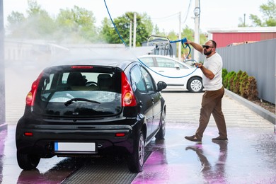 Photo of Man washing auto with high pressure water jet at car wash