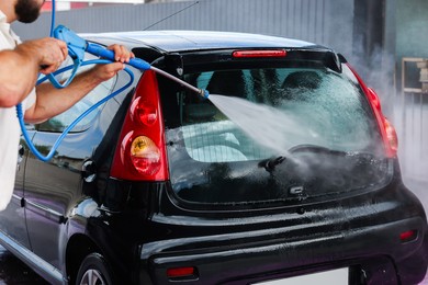 Photo of Man washing auto with high pressure water jet at car wash, closeup