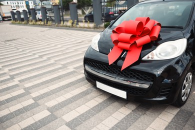 Photo of Dreams come true. New auto with big red bow outdoors, closeup. Space for text