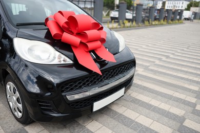 Photo of Dreams come true. New auto with big red bow outdoors, closeup. Space for text