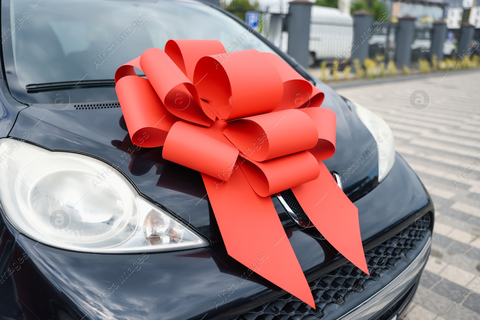 Dreams come true. New auto with big red bow outdoors, closeup Photo of Dreams come true. New auto with big red bow outdoors, closeup