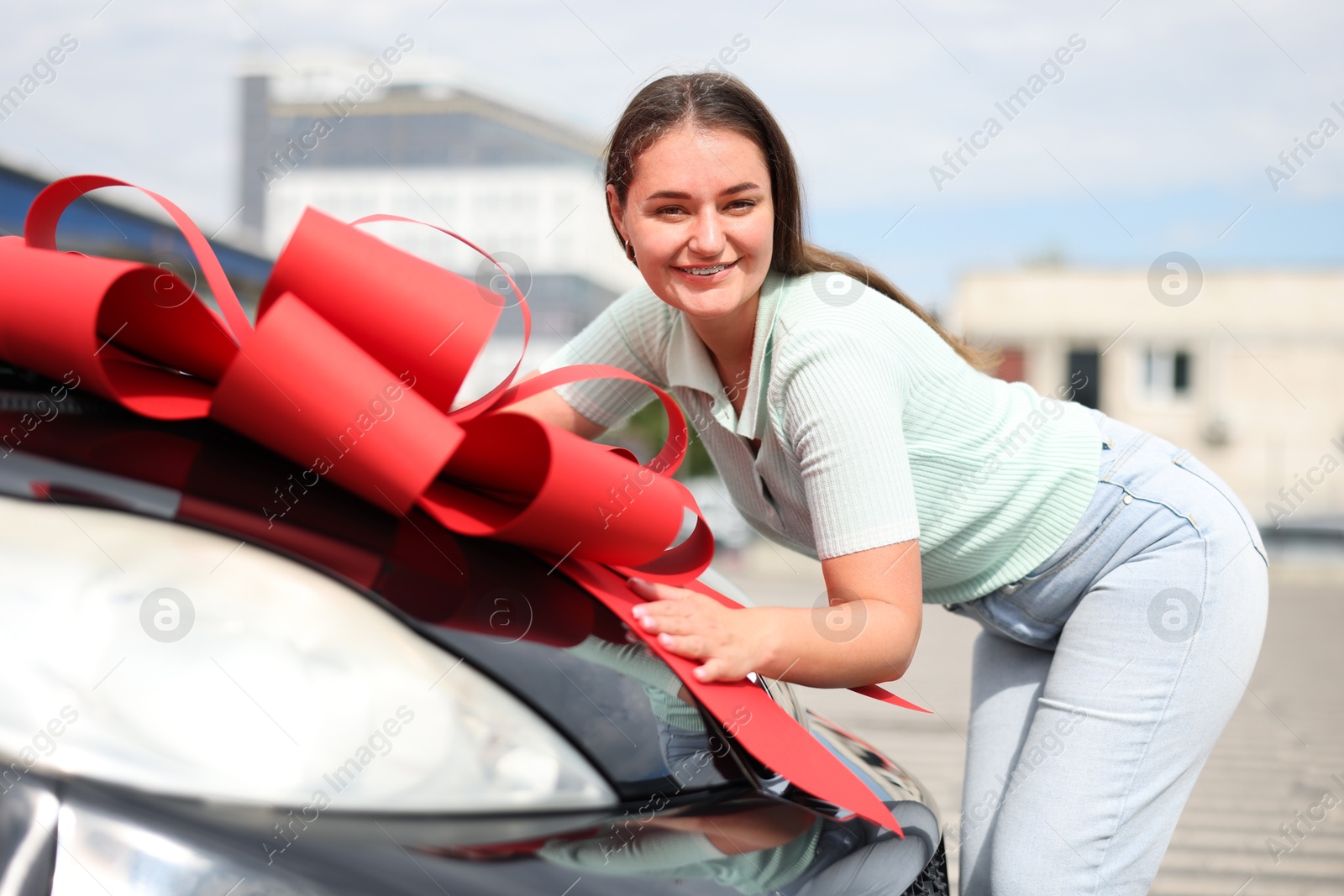 Dreams come true. Woman near her new auto with big red bow outdoors Photo of Dreams come true. Woman near her new auto with big red bow outdoors