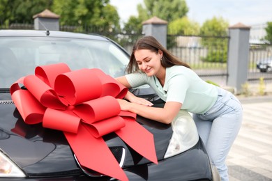 Photo of Dreams come true. Woman near her new auto with big red bow outdoors