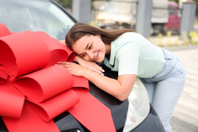 Photo of Dreams come true. Woman near her new auto with big red bow outdoors