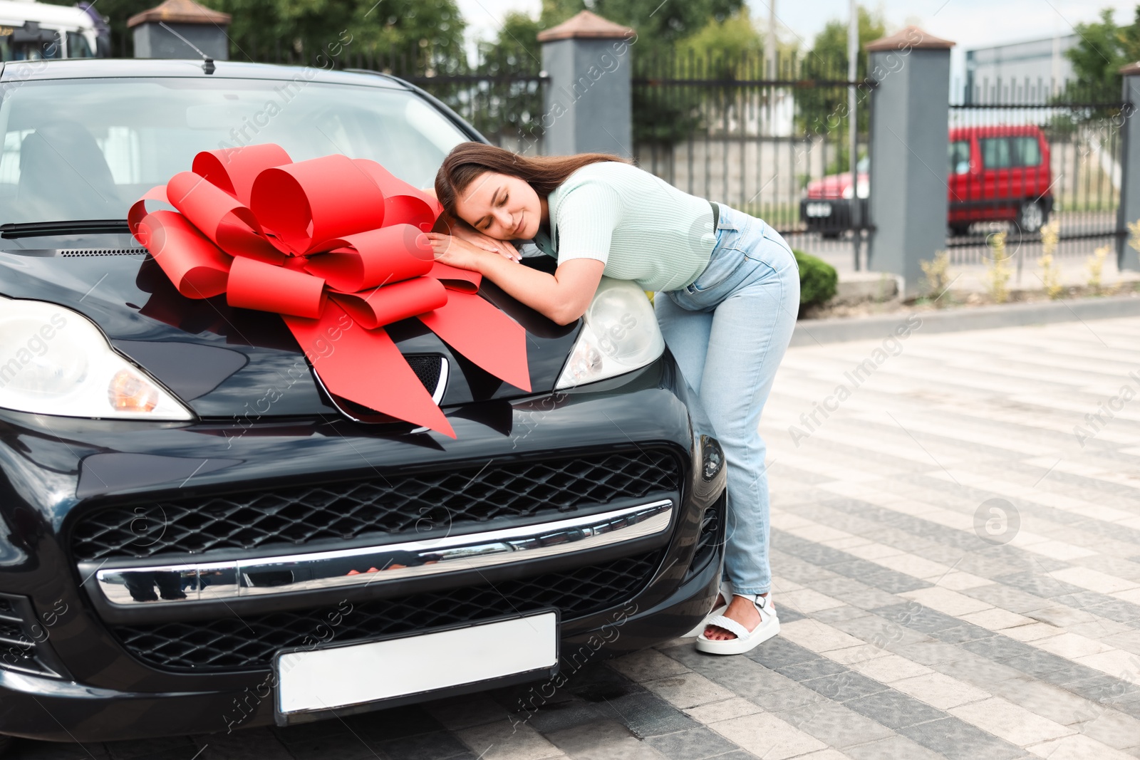 Dreams come true. Woman near her new auto with big red bow outdoors Photo of Dreams come true. Woman near her new auto with big red bow outdoors