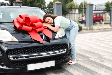 Photo of Dreams come true. Woman near her new auto with big red bow outdoors