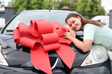 Photo of Dreams come true. Woman near her new auto with big red bow outdoors