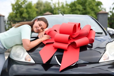 Photo of Dreams come true. Woman near her new auto with big red bow outdoors