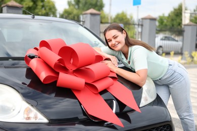 Photo of Dreams come true. Woman near her new auto with big red bow outdoors
