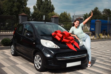 Photo of Dreams come true. Woman near her new auto with big red bow outdoors