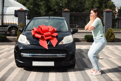 Photo of Dreams come true. Woman near her new auto with big red bow outdoors