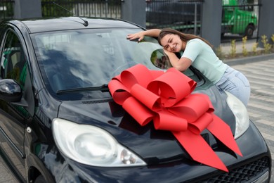 Photo of Dreams come true. Woman near her new auto with big red bow outdoors