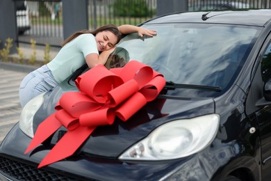 Photo of Dreams come true. Woman near her new auto with big red bow outdoors