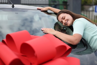 Photo of Dreams come true. Woman near her new auto with big red bow outdoors