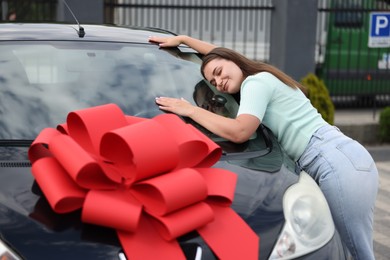 Photo of Dreams come true. Woman near her new auto with big red bow outdoors