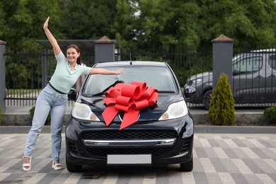 Photo of Dreams come true. Woman near her new auto with big red bow outdoors