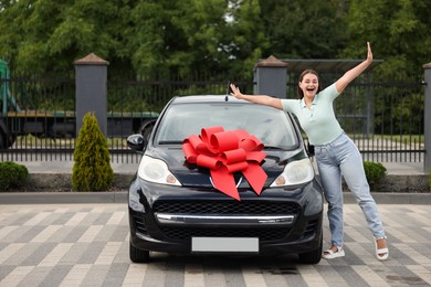 Photo of Dreams come true. Woman near her new auto with big red bow outdoors
