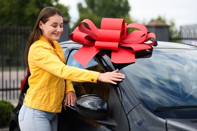 Photo of Dreams come true. Woman near her new auto with big red bow outdoors