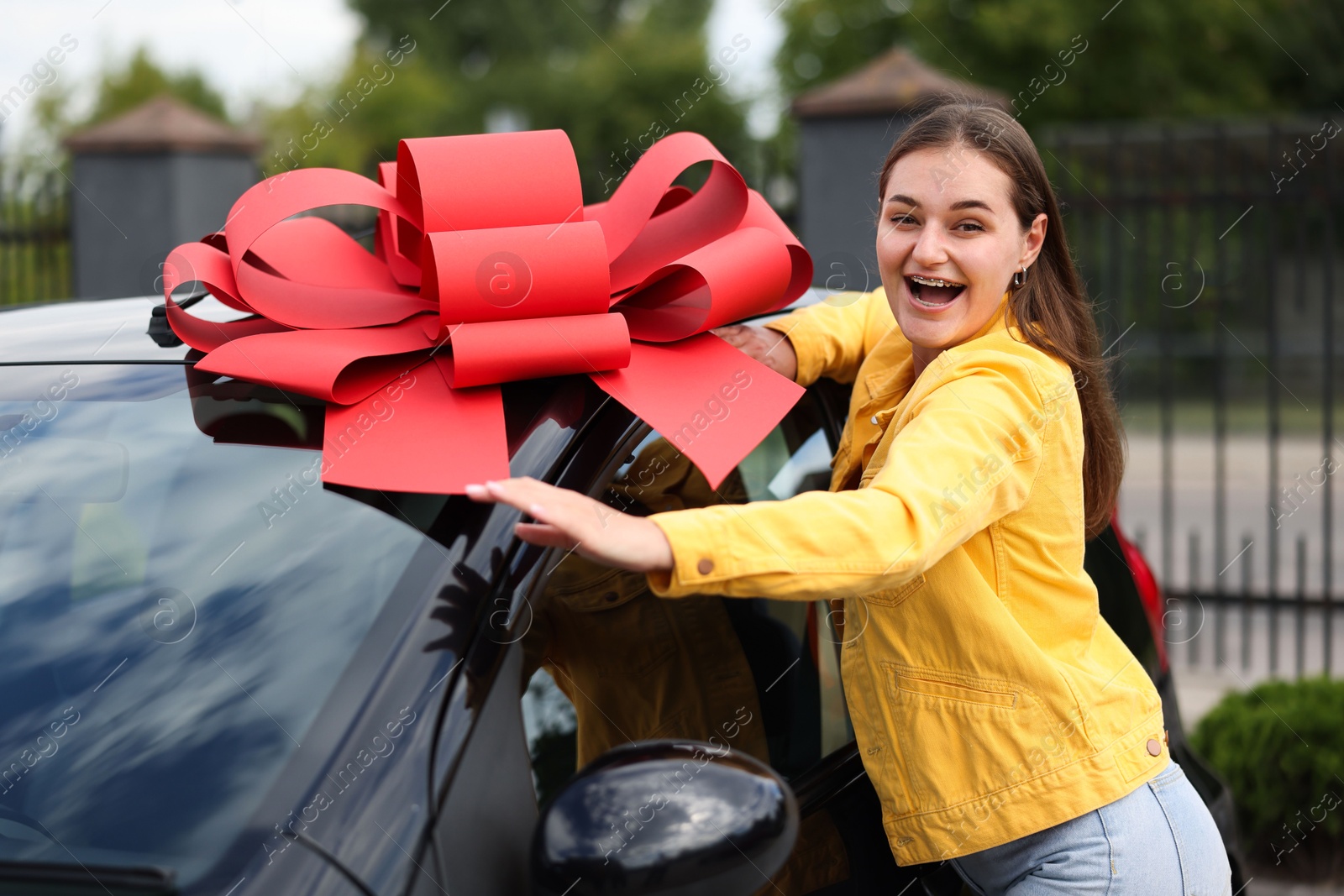 Dreams come true. Woman near her new auto with big red bow outdoors Photo of Dreams come true. Woman near her new auto with big red bow outdoors