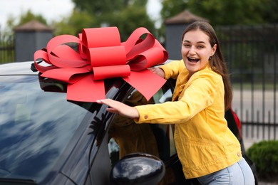 Photo of Dreams come true. Woman near her new auto with big red bow outdoors