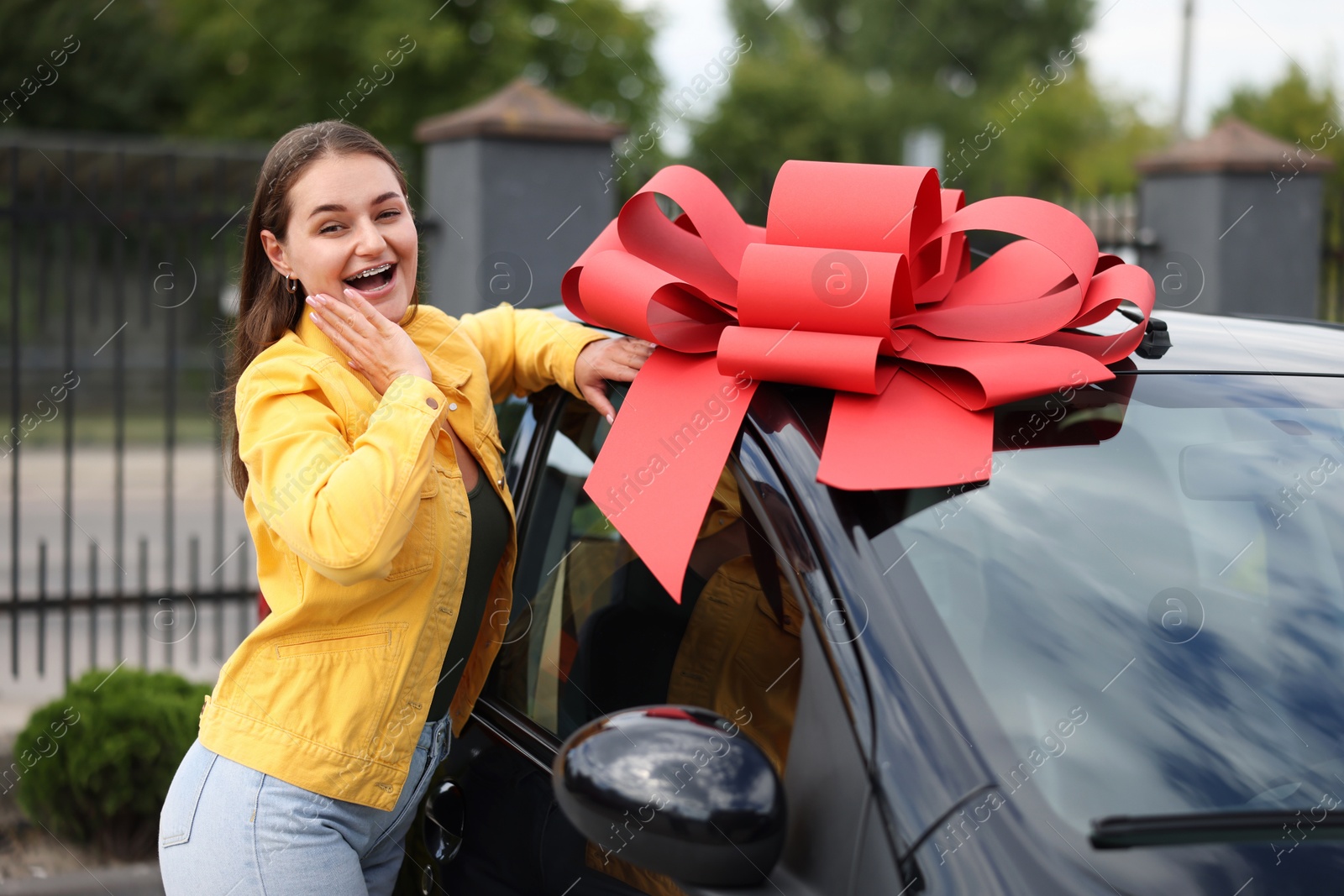 Dreams come true. Woman near her new auto with big red bow outdoors Photo of Dreams come true. Woman near her new auto with big red bow outdoors