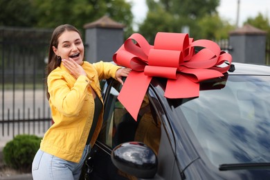 Photo of Dreams come true. Woman near her new auto with big red bow outdoors