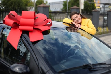 Photo of Dreams come true. Woman near her new auto with big red bow outdoors