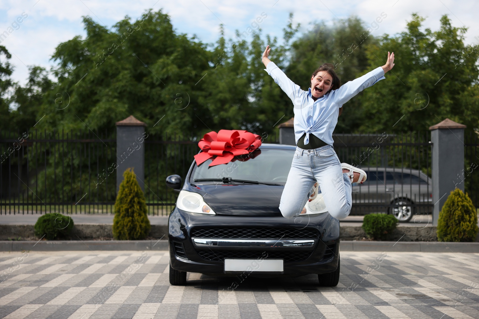 Dreams come true. Woman jumping near her new auto with big red bow outdoors Photo of Dreams come true. Woman jumping near her new auto with big red bow outdoors