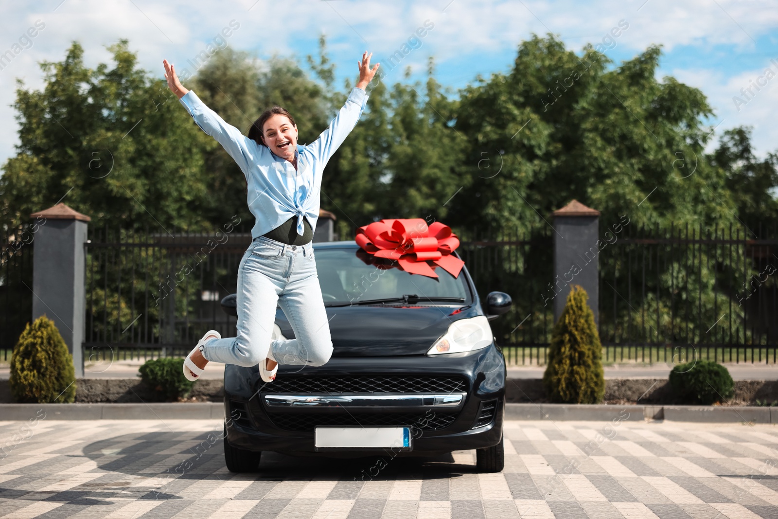 Dreams come true. Woman jumping near her new auto with big red bow outdoors Photo of Dreams come true. Woman jumping near her new auto with big red bow outdoors