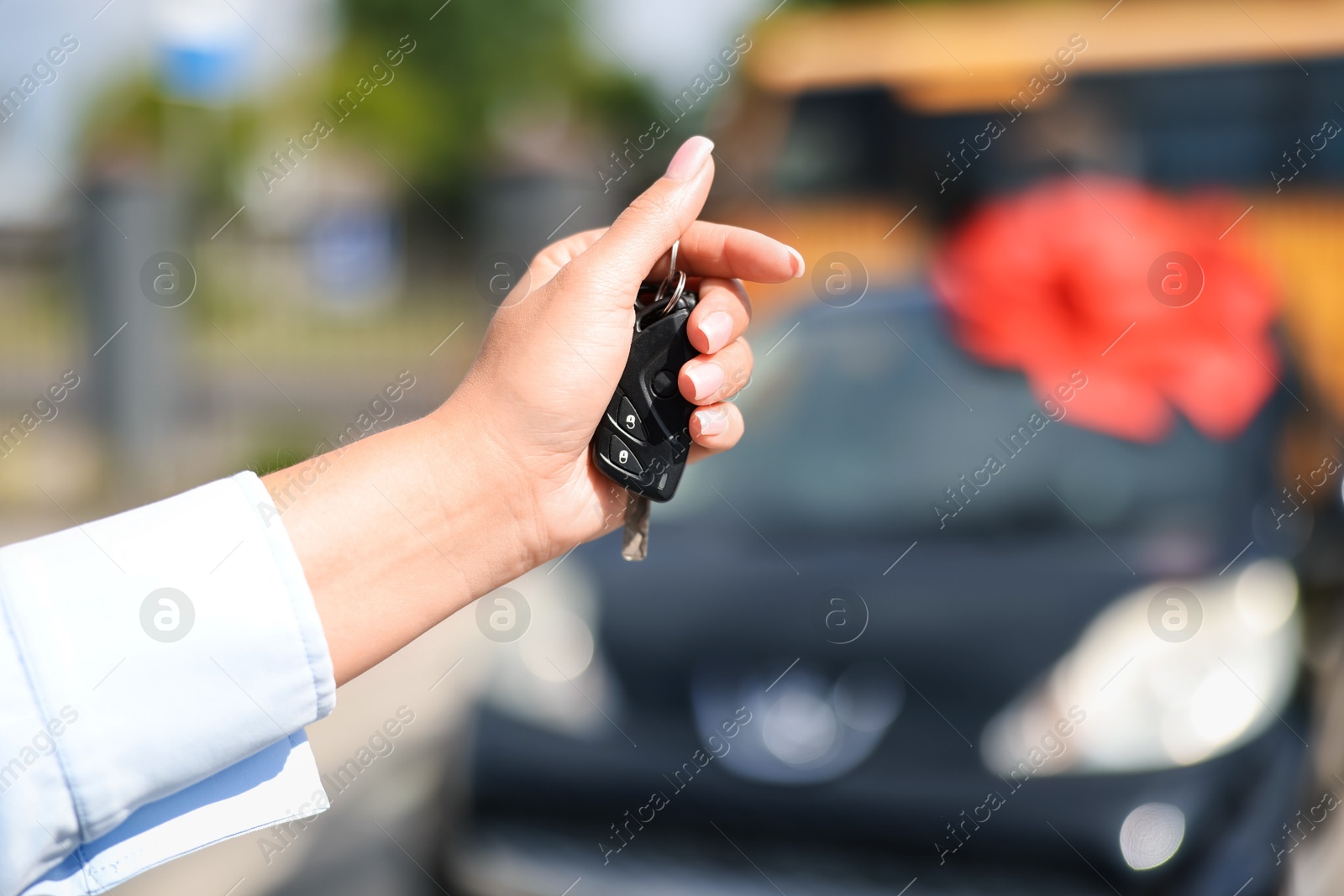 Dreams come true. Woman holding car key near her new auto with big red bow outdoors, closeup Photo of Dreams come true. Woman holding car key near her new auto with big red bow outdoors, closeup
