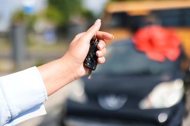 Photo of Dreams come true. Woman holding car key near her new auto with big red bow outdoors, closeup